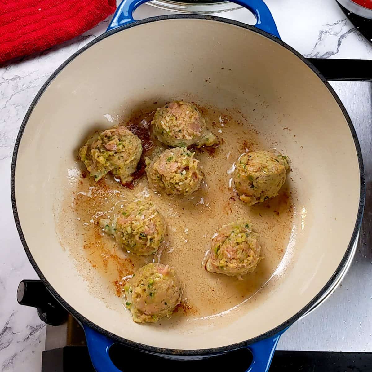 Homemade curry turkey meatballs sizzling in a vibrant blue pot, ready for soup.