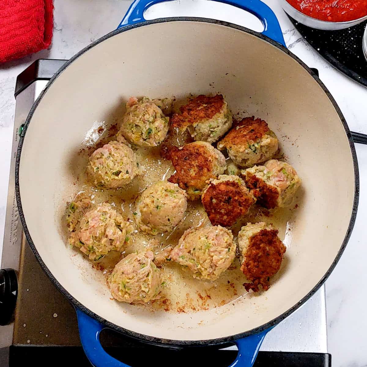 Sizzling curry turkey meatballs in a vibrant blue Dutch oven on the stovetop.