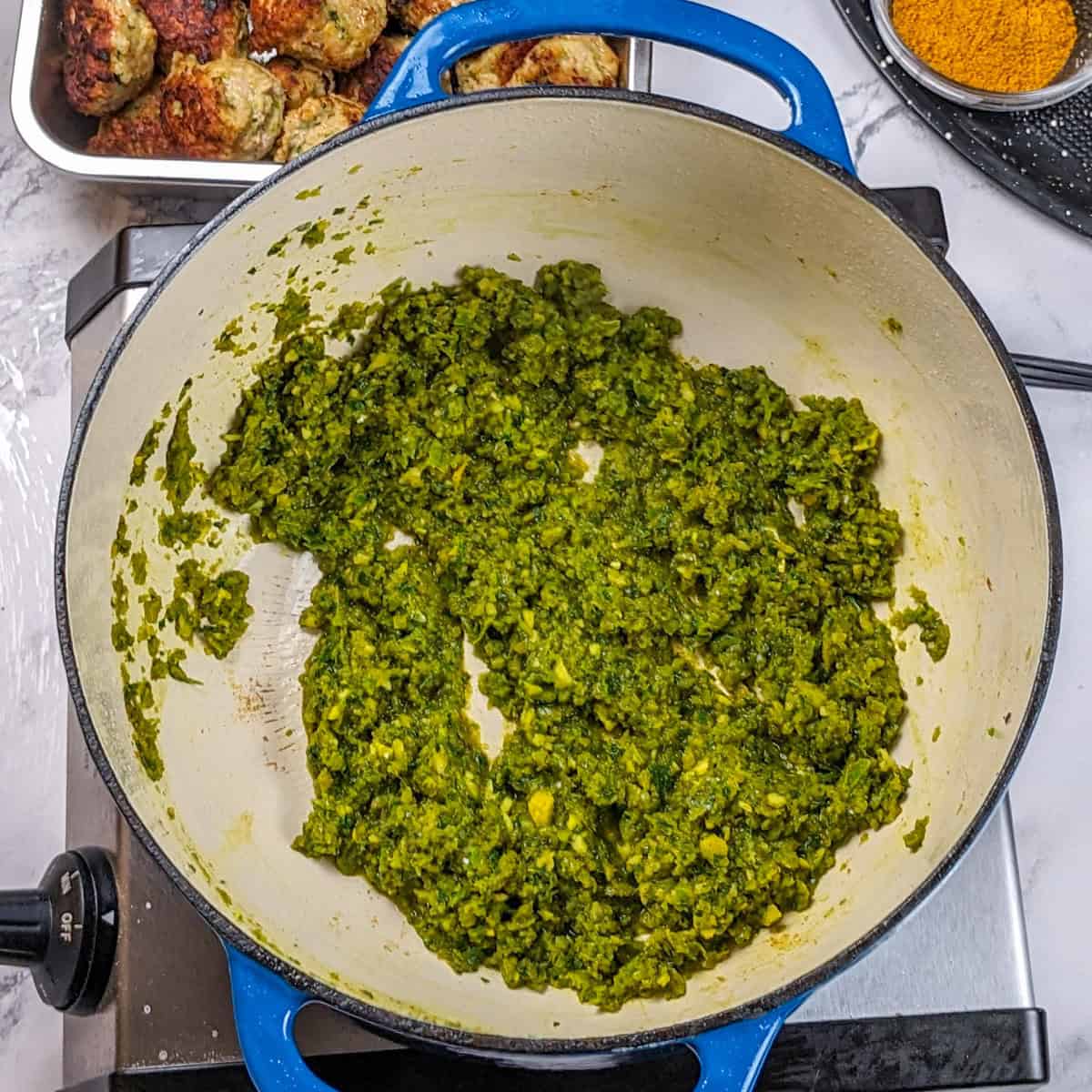 Vibrant green seasoning paste in a blue-handled cast-iron pot.