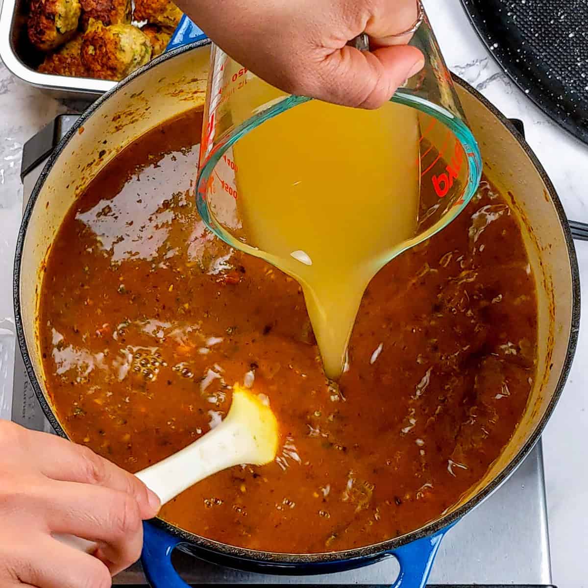 Cooking curry turkey meatball soup, pouring broth into a pot for enhanced flavor.