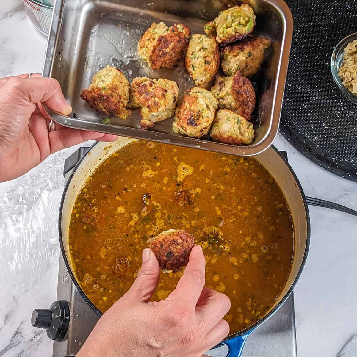 Golden broth simmers in a modern kitchen, as crispy turkey meatballs are added.