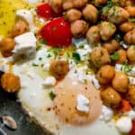 Vibrant eggs and chickpeas skillet topped with feta, red peppers, and fresh herbs.