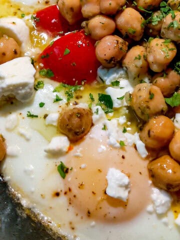 Vibrant eggs and chickpeas skillet topped with feta, red peppers, and fresh herbs.