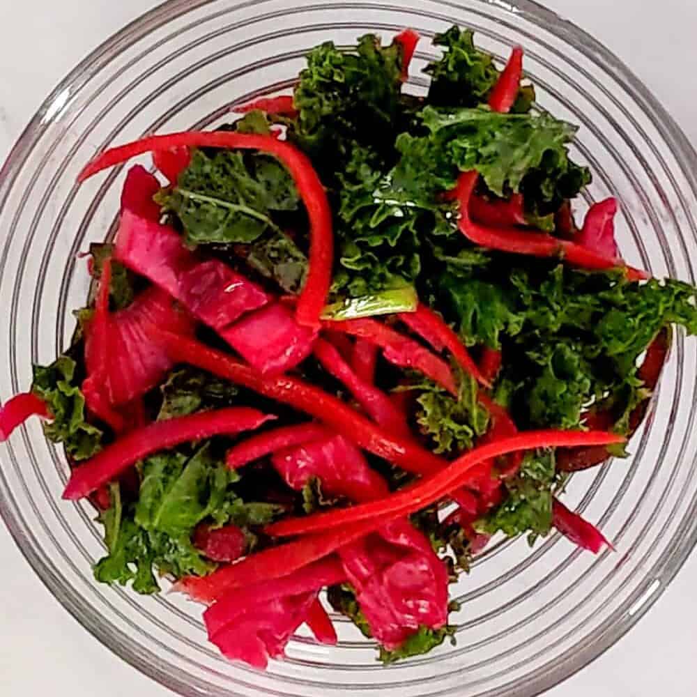 Fresh kale salad with vibrant red bell peppers in a clear bowl, perfect for healthy eating.