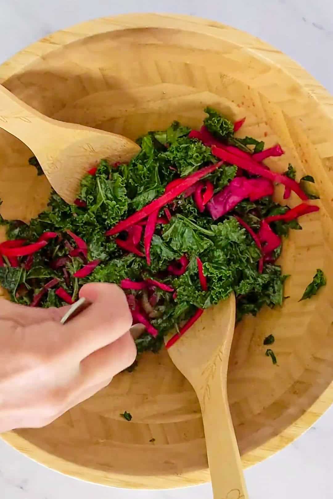 Vibrant kale salad with red beet strips, mixed with wooden utensils in a rustic bowl.