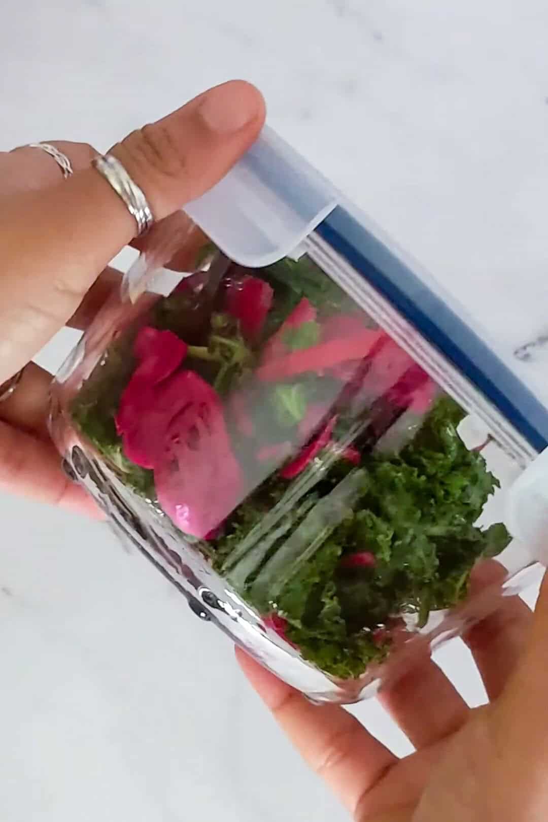 Vibrant kale and rose petals in a sealed glass container, highlighting fresh culinary creativity.