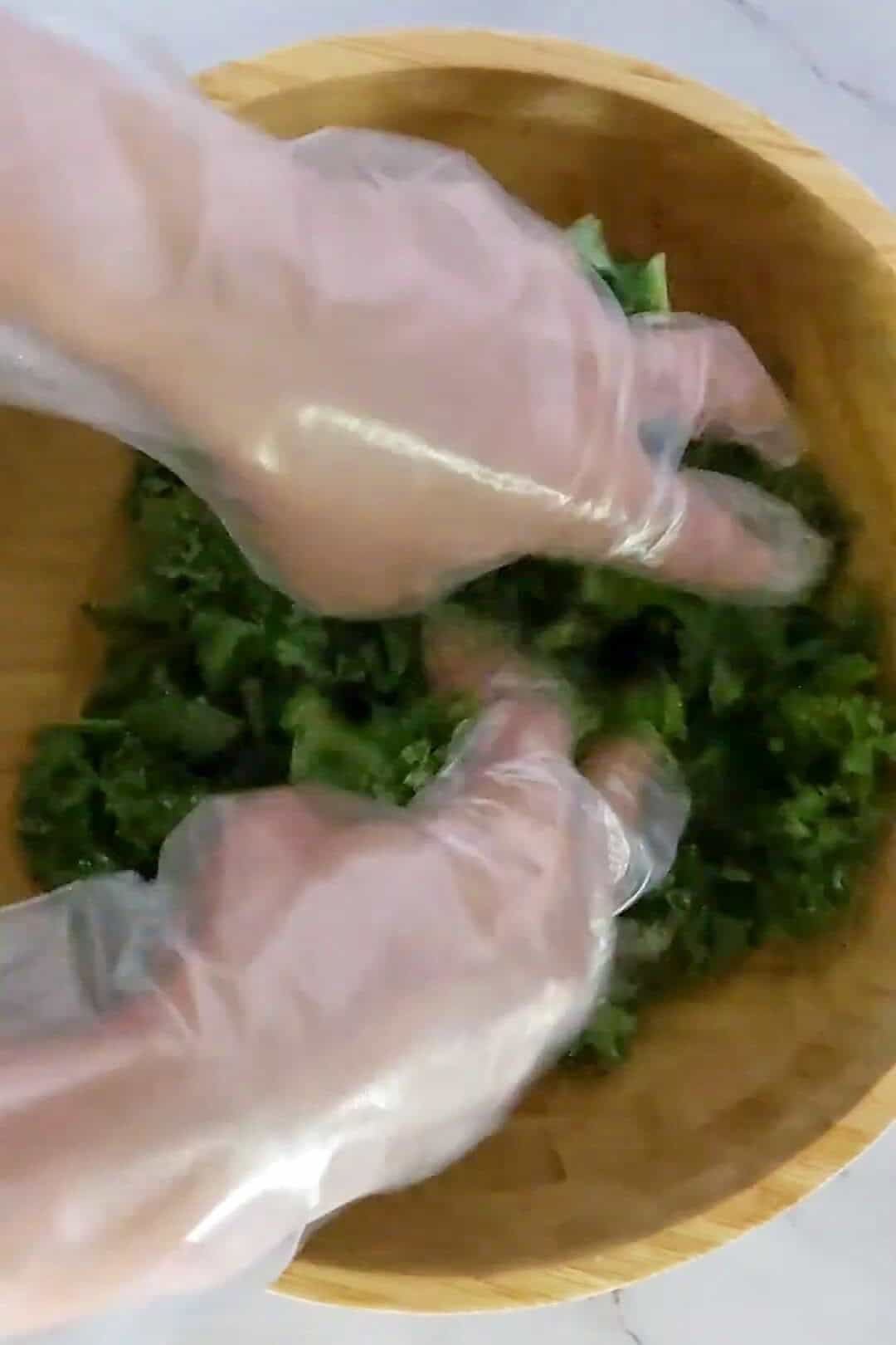 Hands in gloves mixing fresh kale in a wooden bowl, emphasizing healthy food preparation.