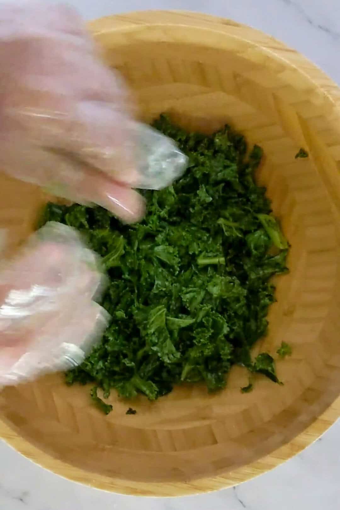 Freshly chopped kale being massaged for flavor enhancement in a bamboo bowl.