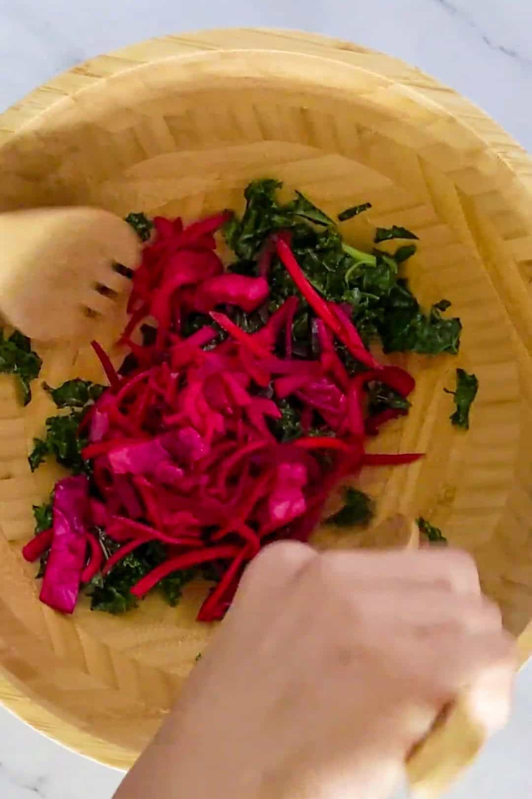 Vibrant salad preparation featuring fresh greens and shredded pink vegetables in a wooden bowl.