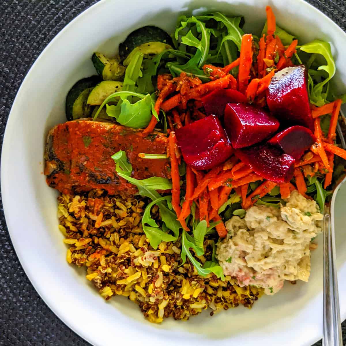 Colorful salmon bowl with spiced brown basmati rice, fresh greens, and vibrant vegetables.