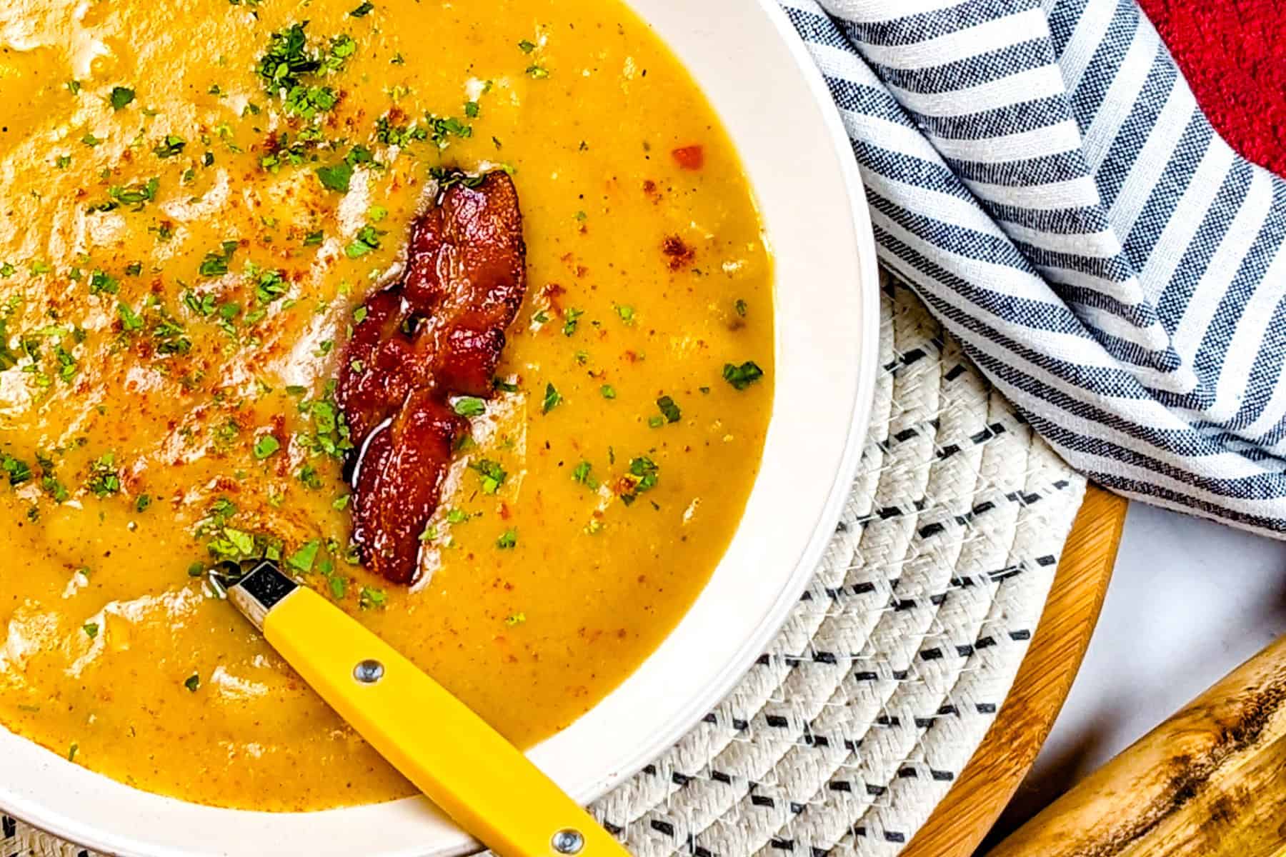 Creamy bacon potato leek chowder garnished with herbs, featuring a glossy, inviting soup bowl.