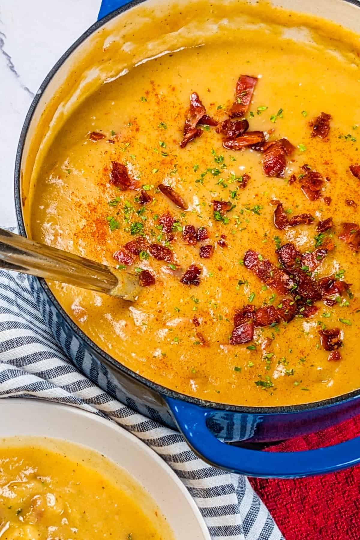 Creamy spicy bacon potato leek chowder in a vibrant blue pot, garnished with herbs.