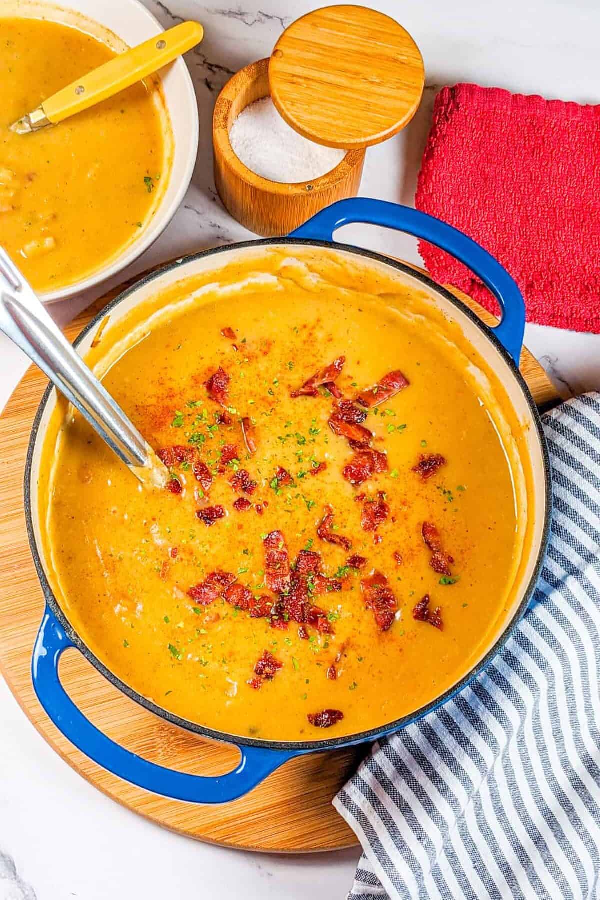 Creamy spicy bacon potato leek chowder served in a vibrant blue pot and bowl.