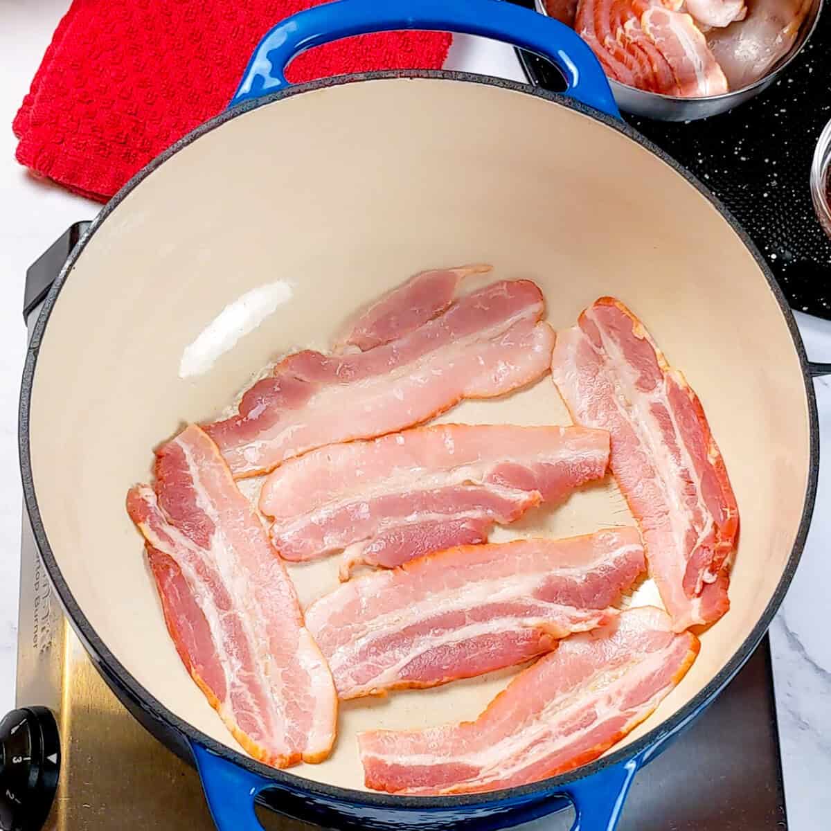 Bacon sizzling in a vibrant Dutch oven for Spicy Bacon Potato Leek Chowder preparation.