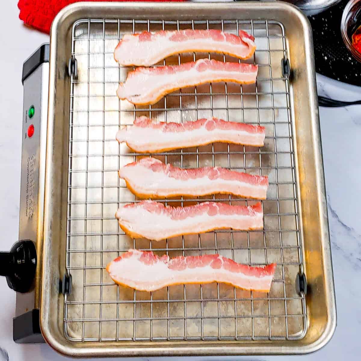 Raw bacon strips on a wire rack, ready for cooking in a metal baking tray.