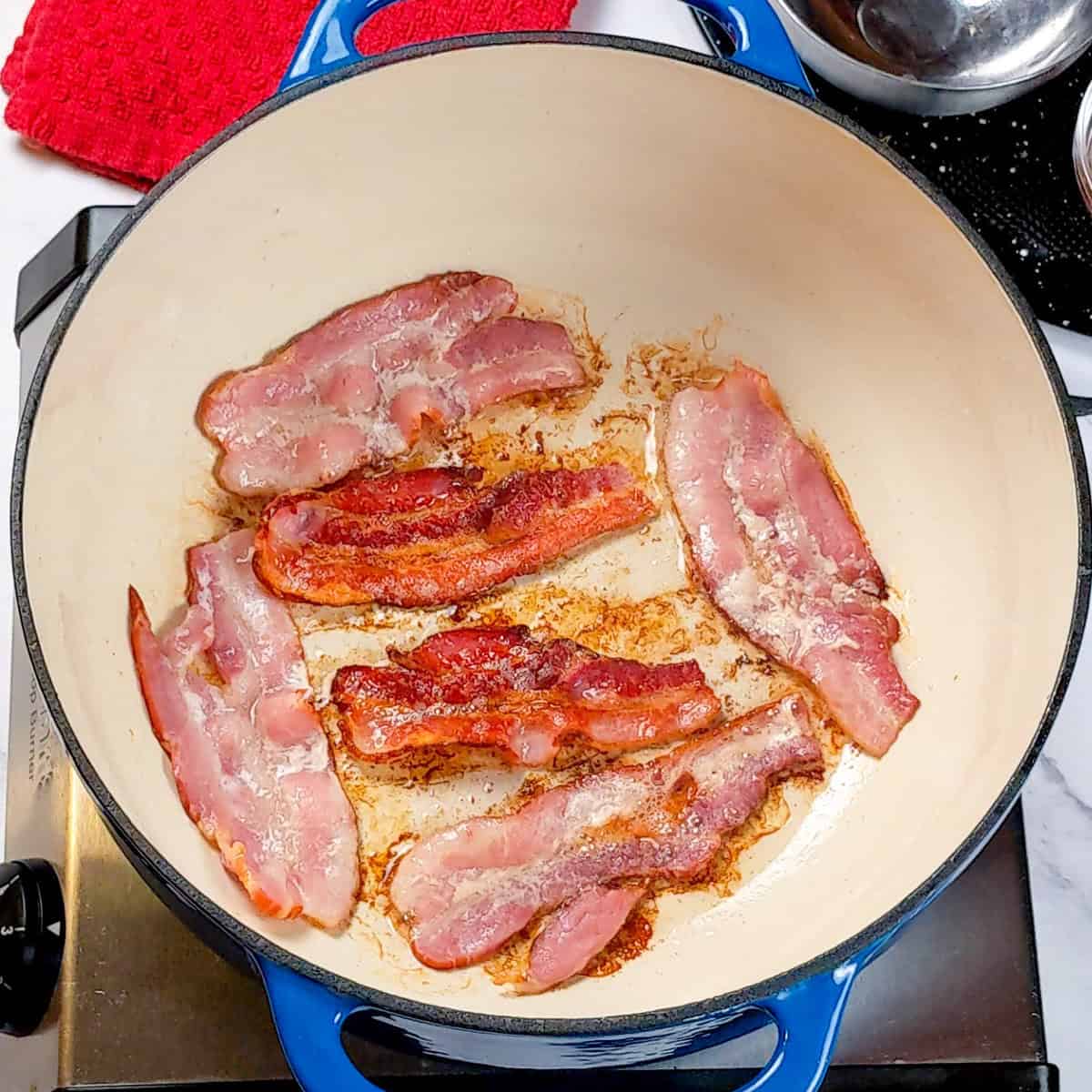 Sizzling bacon in a blue Dutch oven for spicy bacon potato leek chowder.