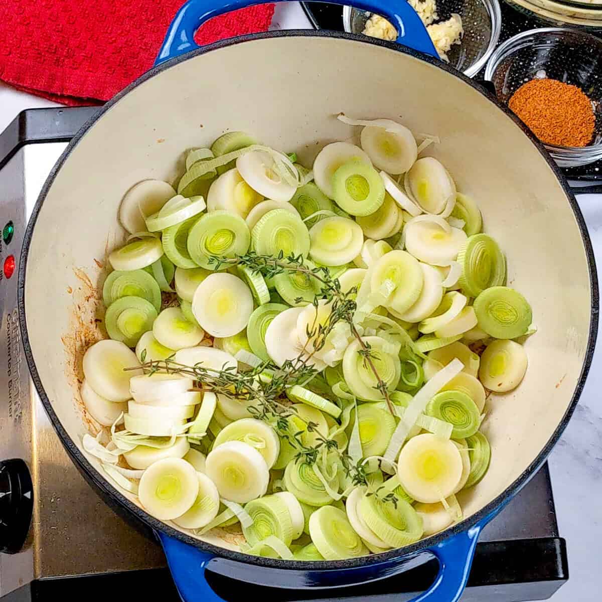 Fresh leeks and thyme prepared for Spicy Bacon Potato Leek Chowder in a blue pot.