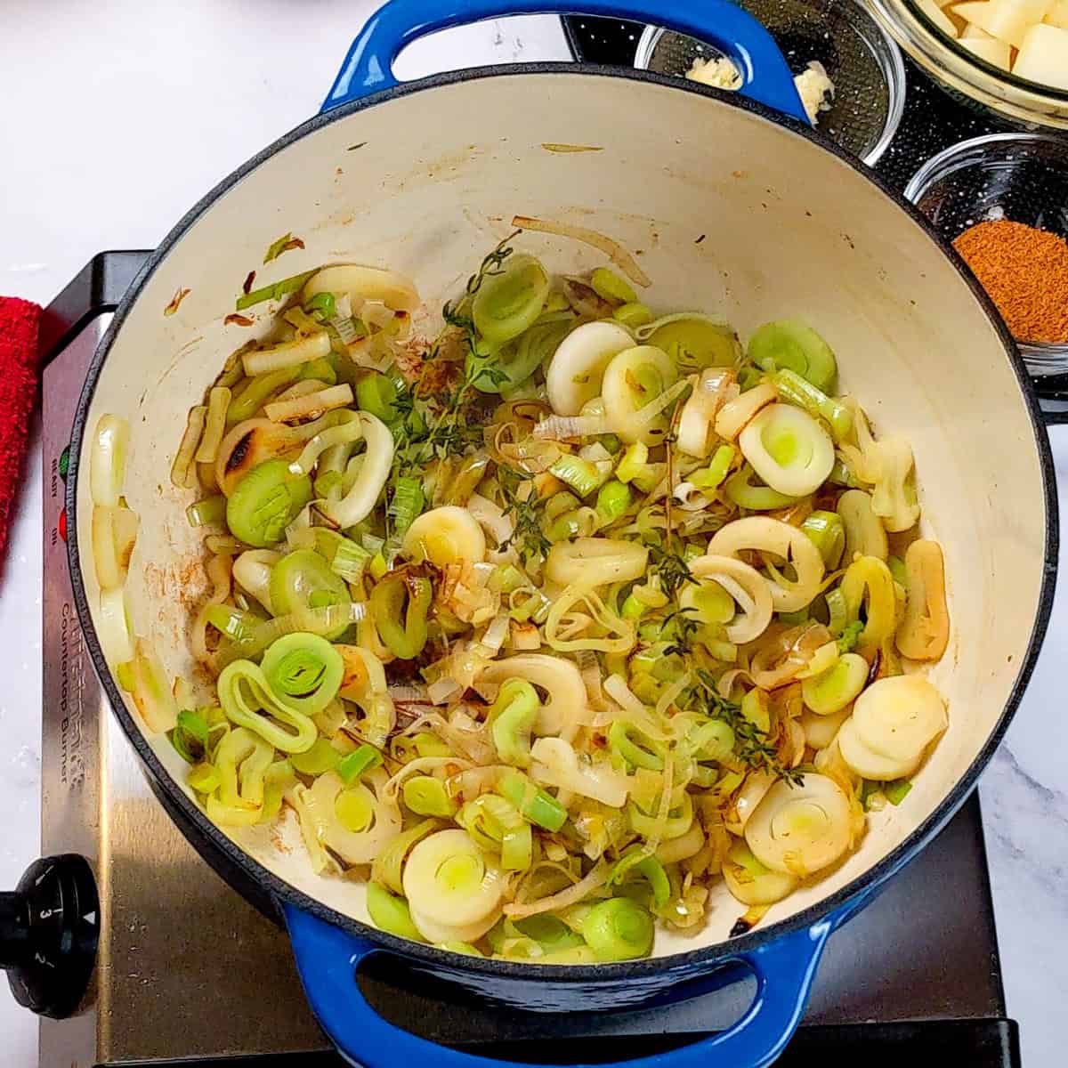 Sautéed leeks and onions in a blue Dutch oven for Spicy Bacon Potato Leek Chowder.