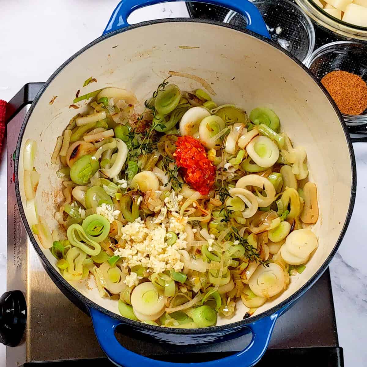 Sautéed leeks, thyme, calabrian chlies and garlic in a blue Dutch oven for Spicy Bacon Potato Leek Chowder.