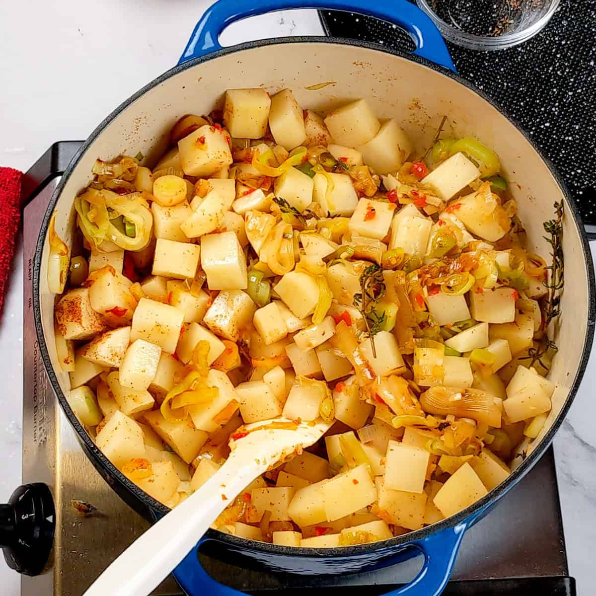 Colorful sautéed potatoes and vegetables in a blue pot for Spicy Bacon Potato Leek Chowder.