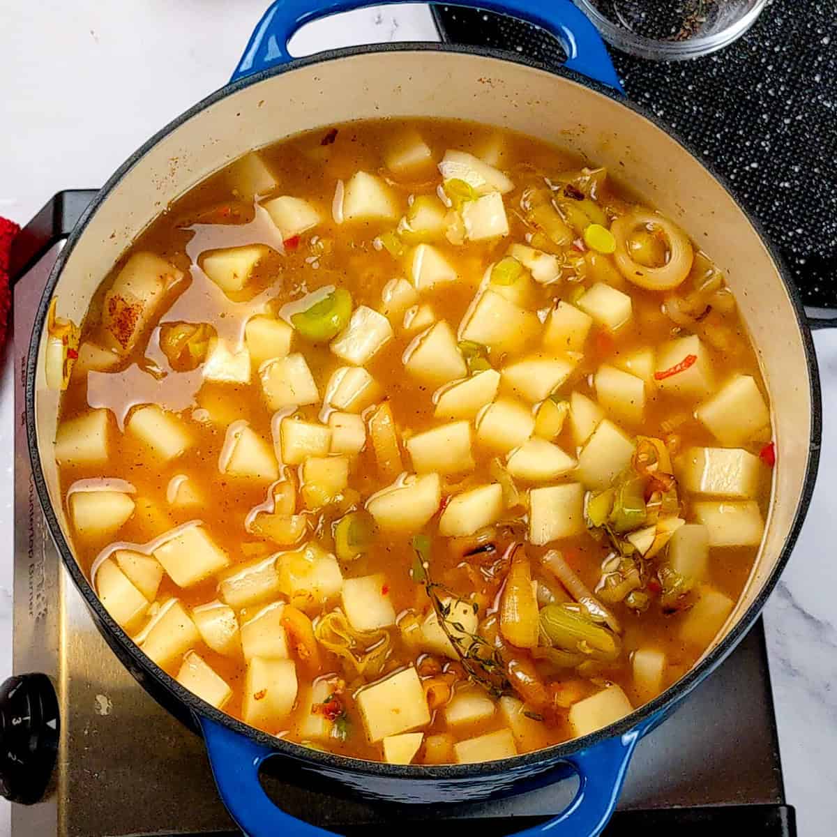 Hearty blue Dutch oven filled with spicy bacon potato leek chowder simmering on the stovetop.