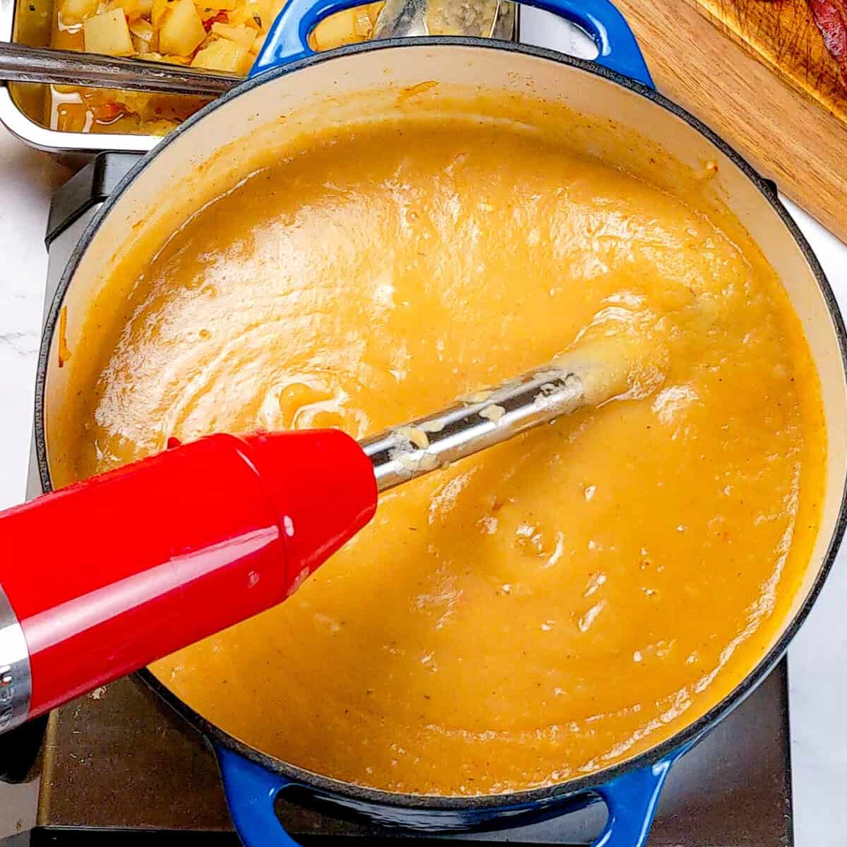 Creamy potato leek chowder blending with red immersion blender in vibrant kitchen scene.