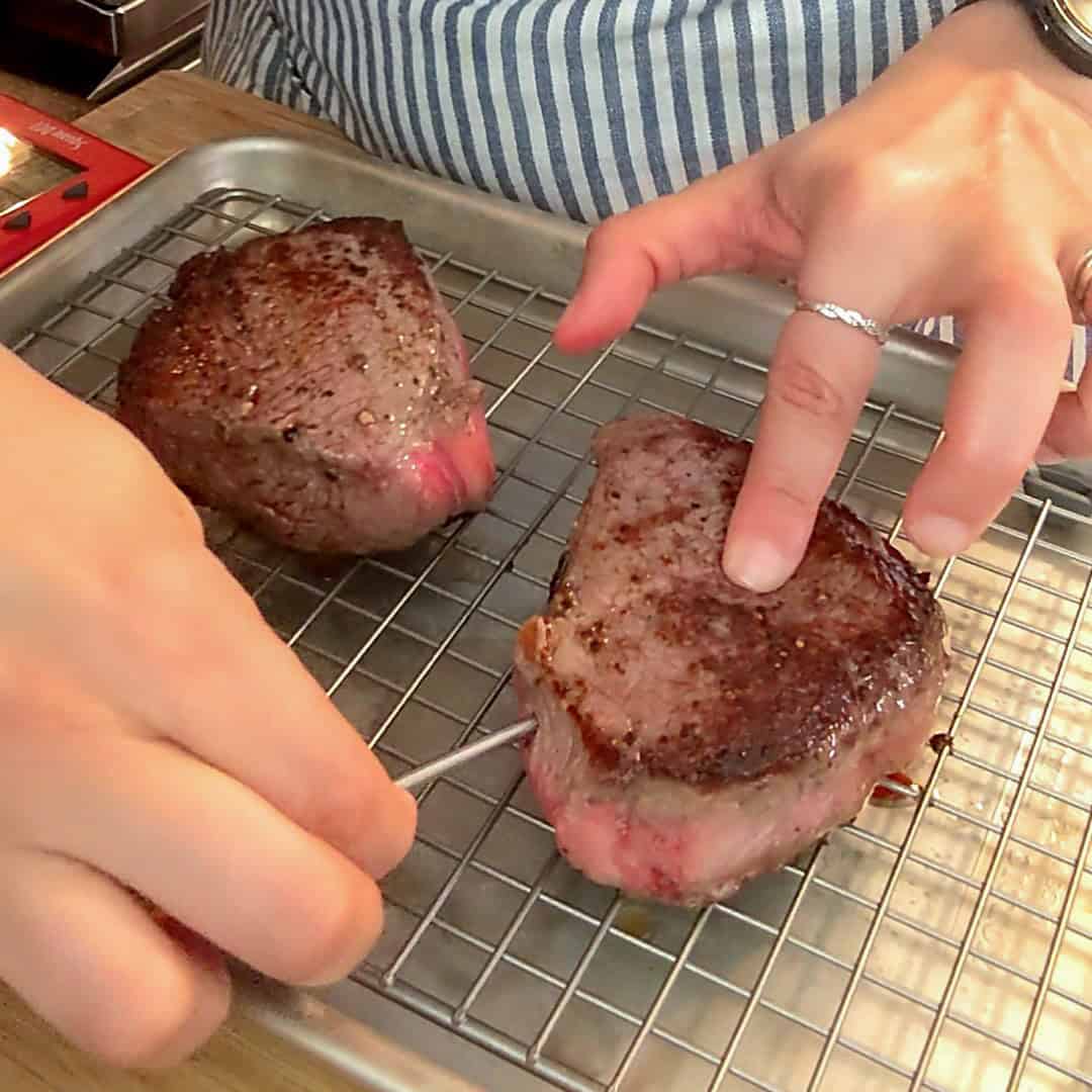 Meat thermometer checks medium-rare steak on a cooling rack in a cozy kitchen.