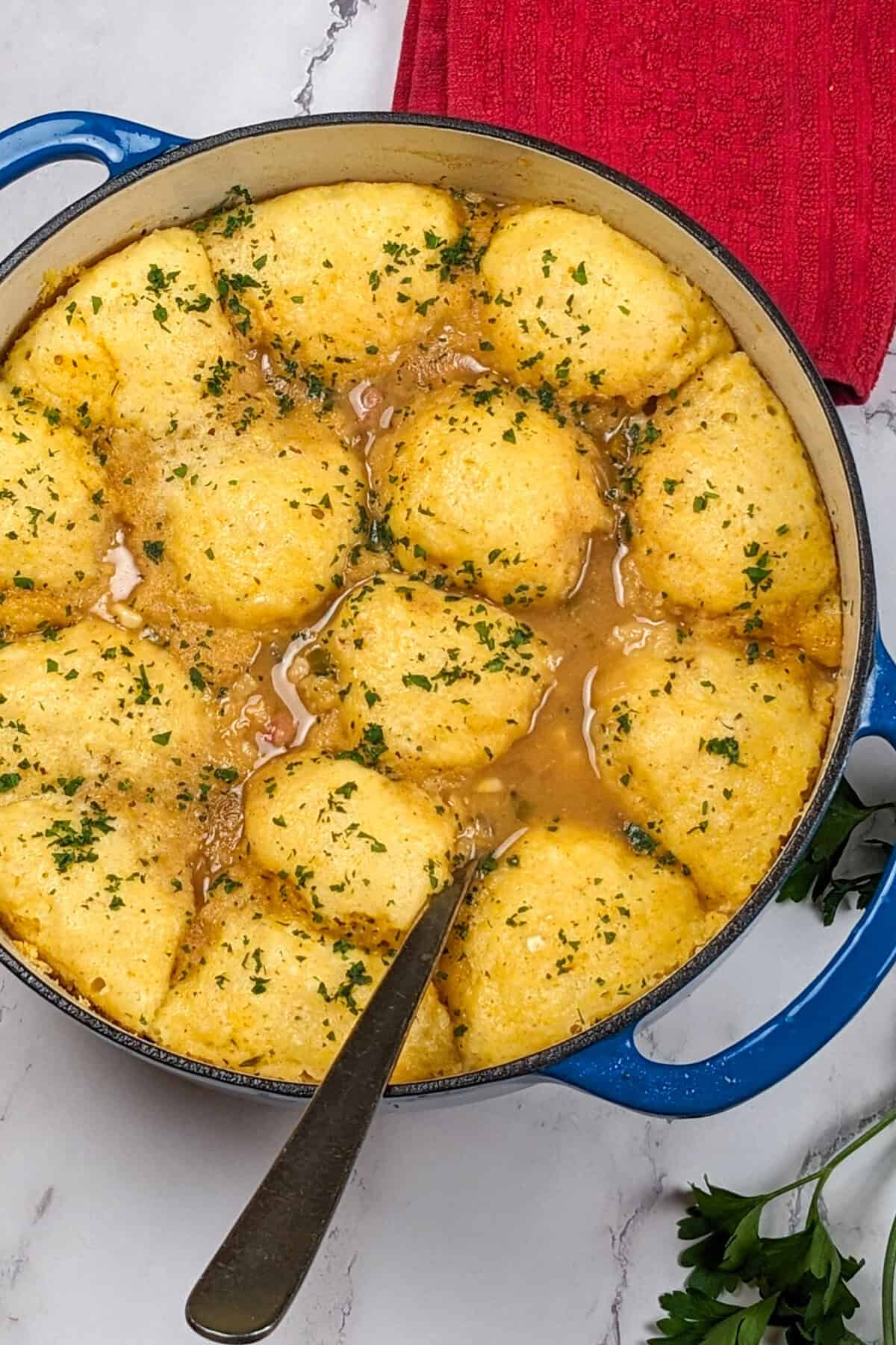 Savory chicken corn chowder dumplings in a blue pot, garnished with fresh parsley.