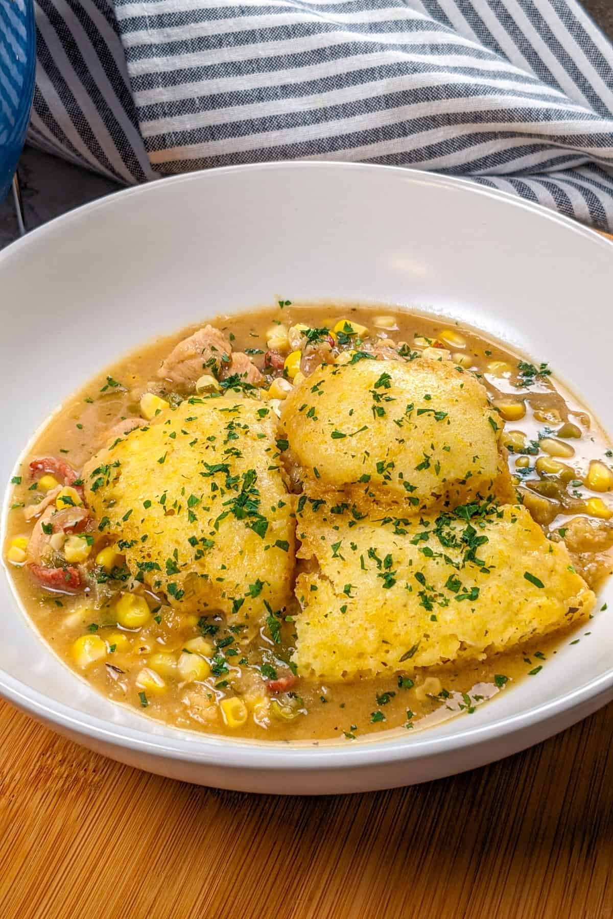 Savory chicken corn chowder with golden cornbread dumplings, garnished with fresh herbs.