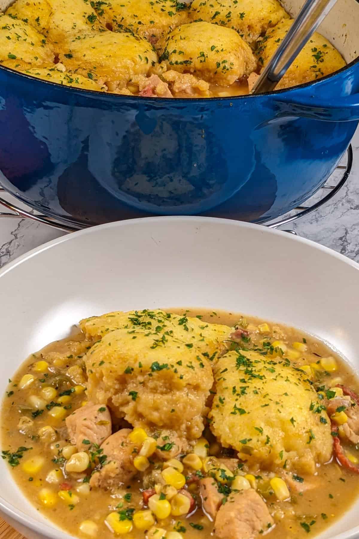 Hearty chicken corn chowder with fluffy dumplings in a rustic blue pot.