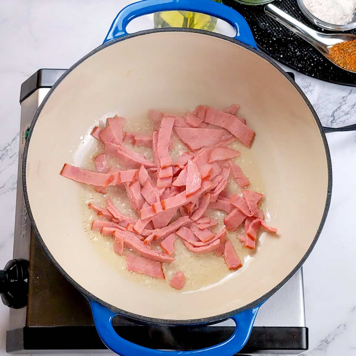 Sizzling turkey bacon strips in a blue pot for chicken corn chowder dumplings preparation.