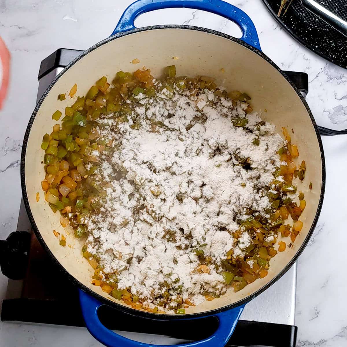 Sautéed vegetables and flour in a blue pot for chicken corn chowder dumplings.