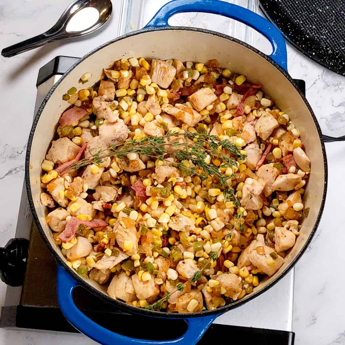 Vibrant chicken corn chowder simmers in a blue pot, showcasing colorful ingredients.