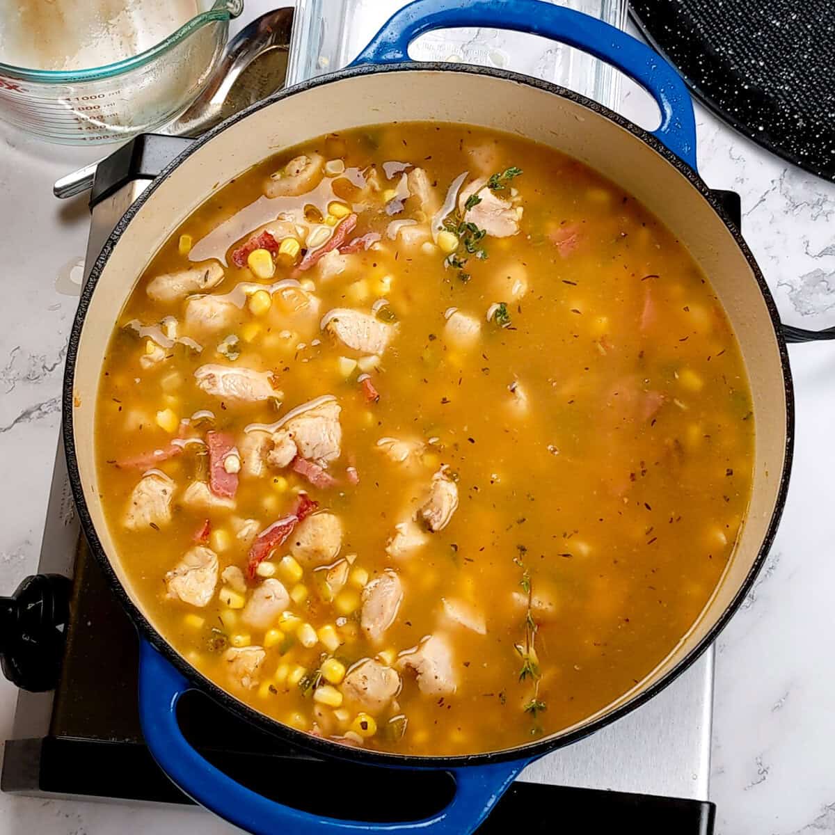 Simmering chicken corn chowder with vibrant herbs and spices in a blue Dutch oven.