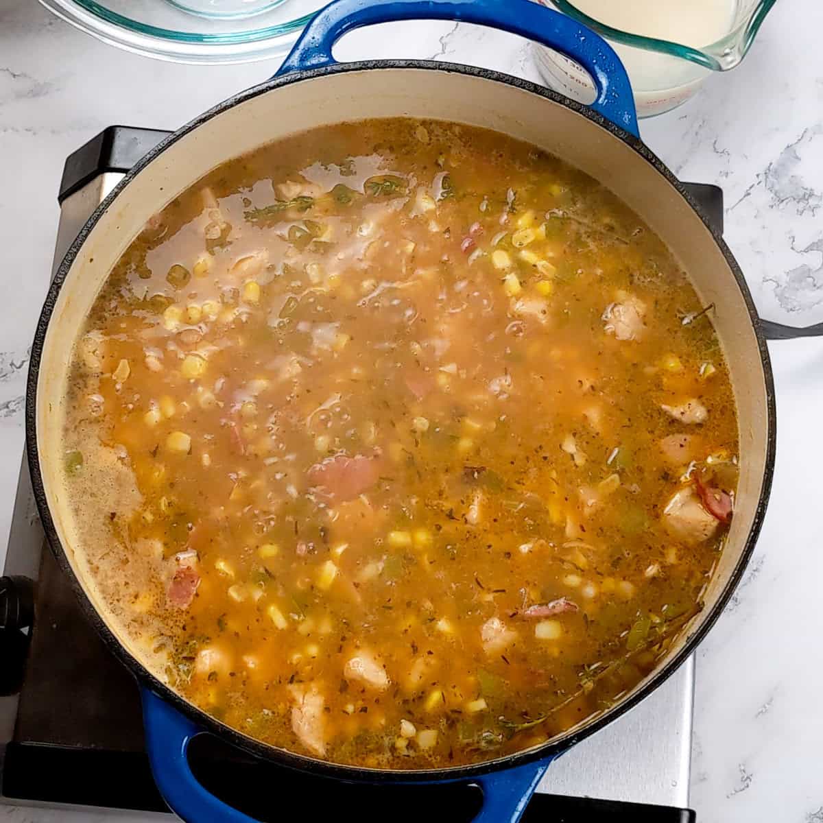 Hearty chicken corn chowder simmering in a blue cast iron pot on a marble stovetop.