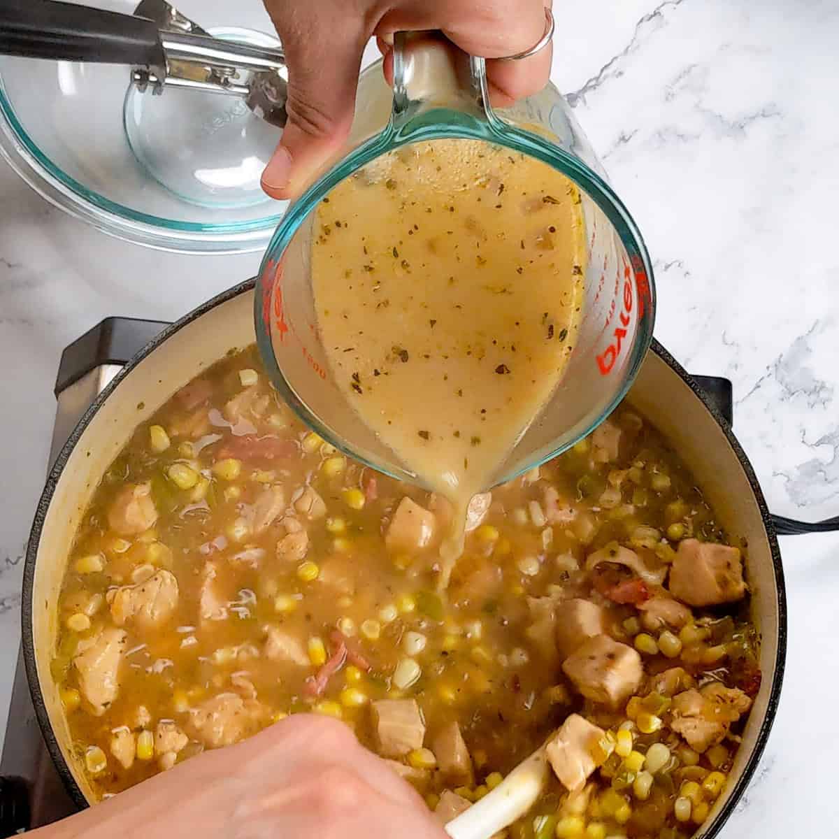 Pouring savory tempered oatmilk broth into a bubbling chicken corn chowder dumplings pot for a flavorful meal.