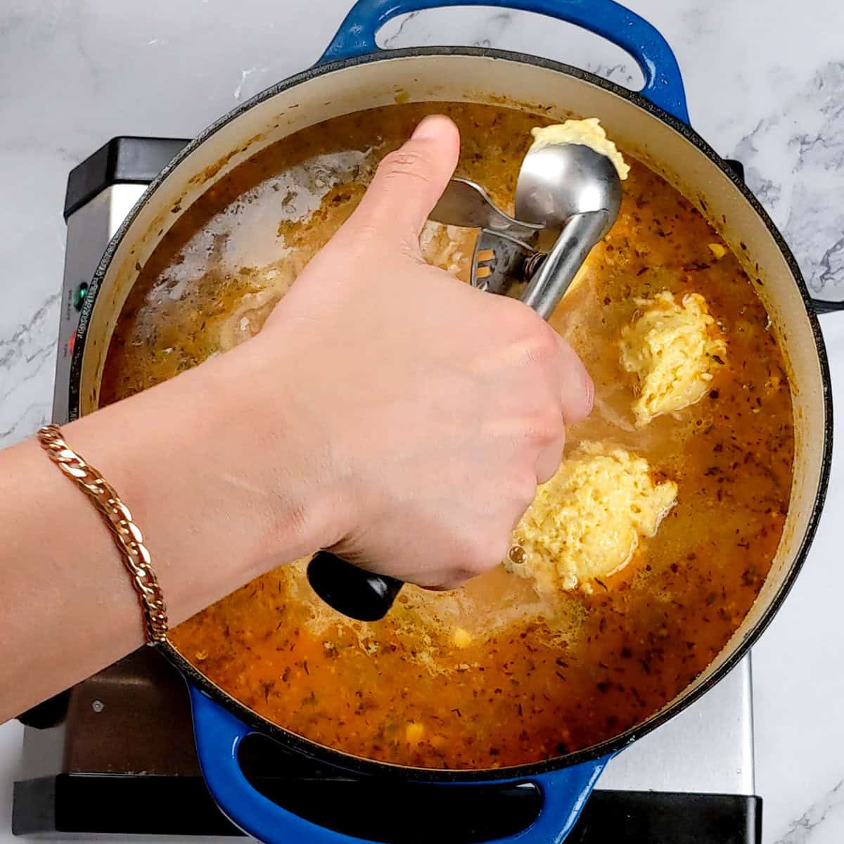 Adding dumplings to chicken corn chowder in a blue cast iron pot on the stovetop.