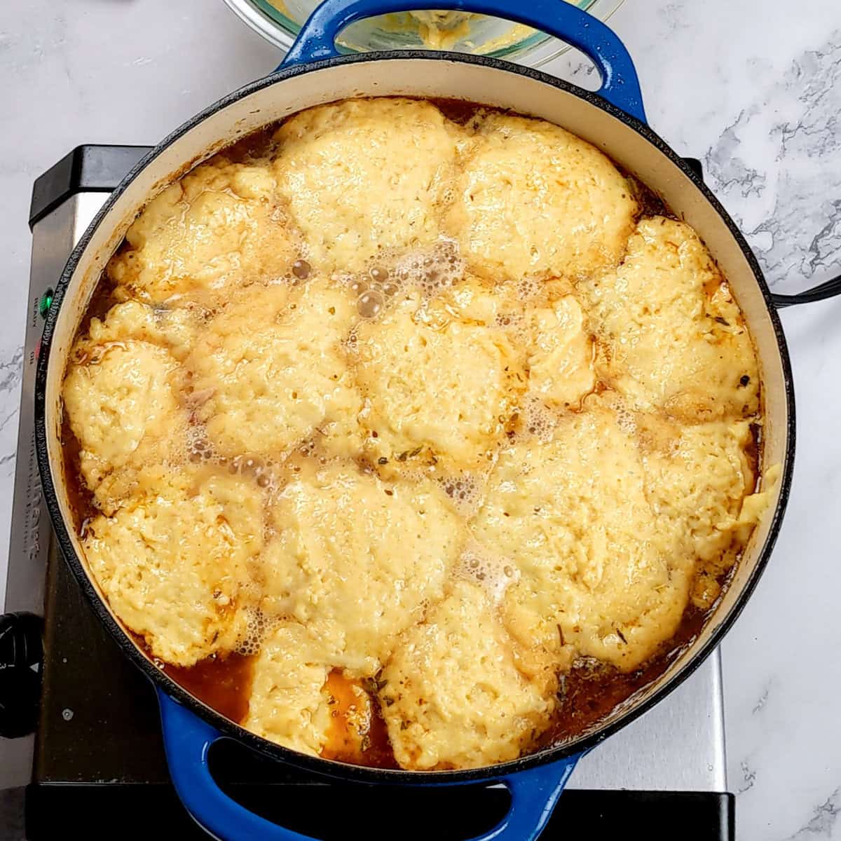 Rich chicken corn chowder with fluffy dumplings in a vibrant blue Dutch oven on stovetop.