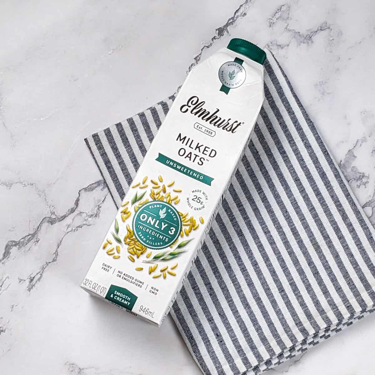 Elmhurst Oat Milk carton on textured surface, showcasing natural ingredients and health benefits.