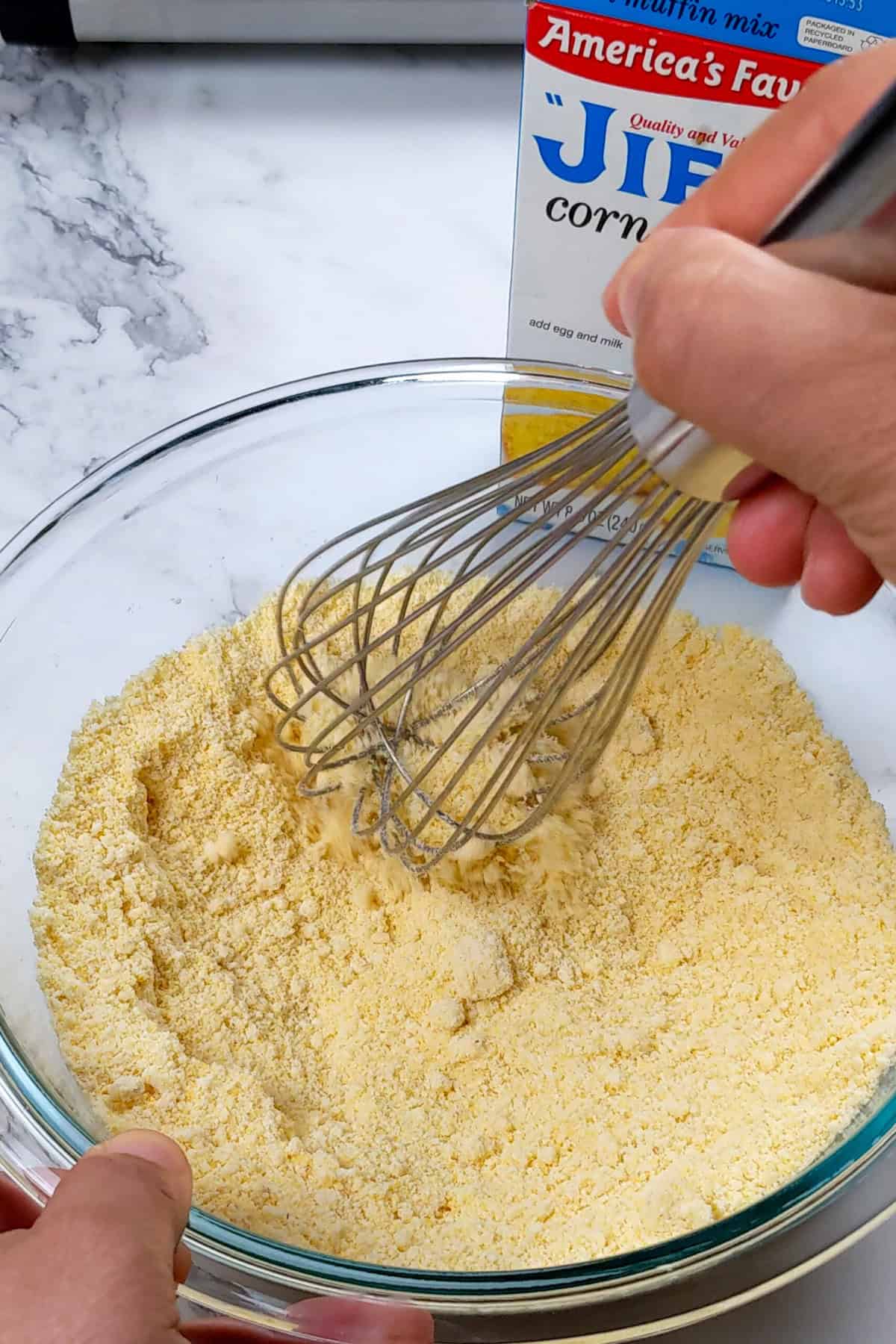 Whisking Jiffy cornbread mix in a glass bowl for fluffy homemade cornbread.