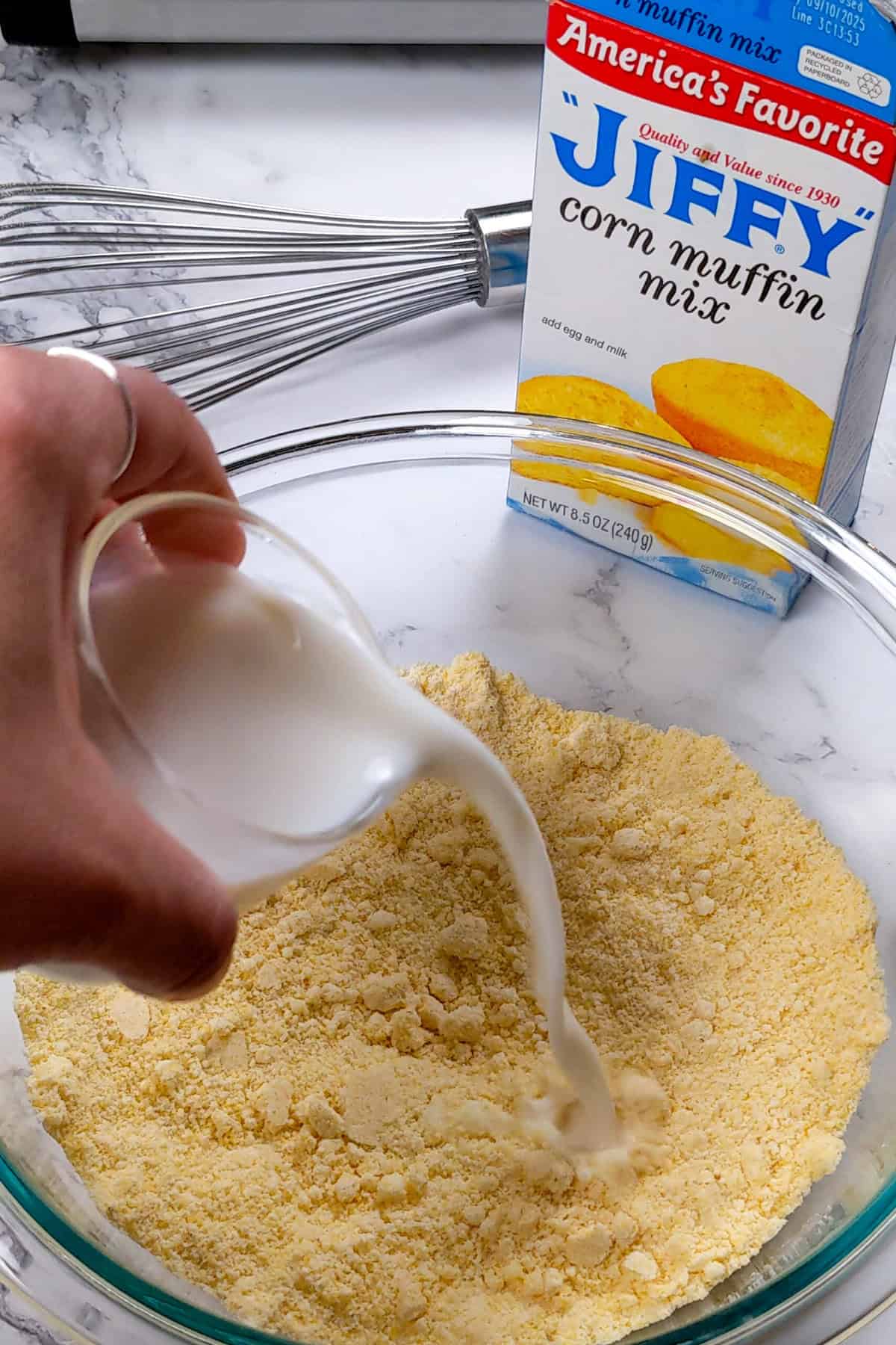 Pouring milk into Jiffy Cornbread Mix for delicious homemade cornbread.