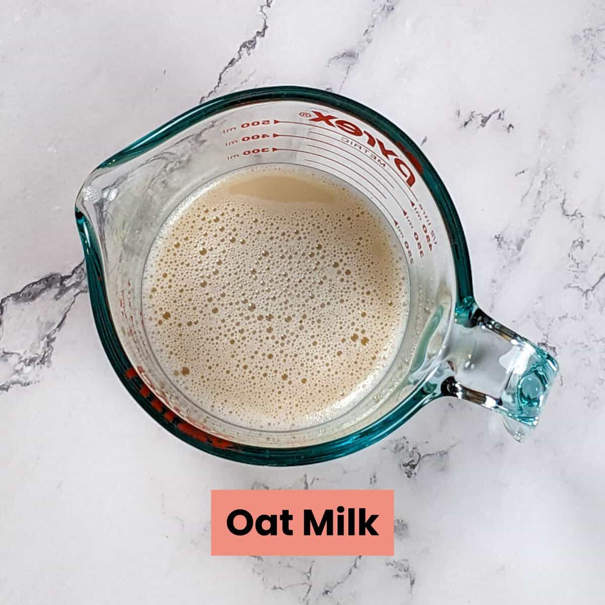 Creamy oat milk in a glass measuring cup on a stylish marble surface.