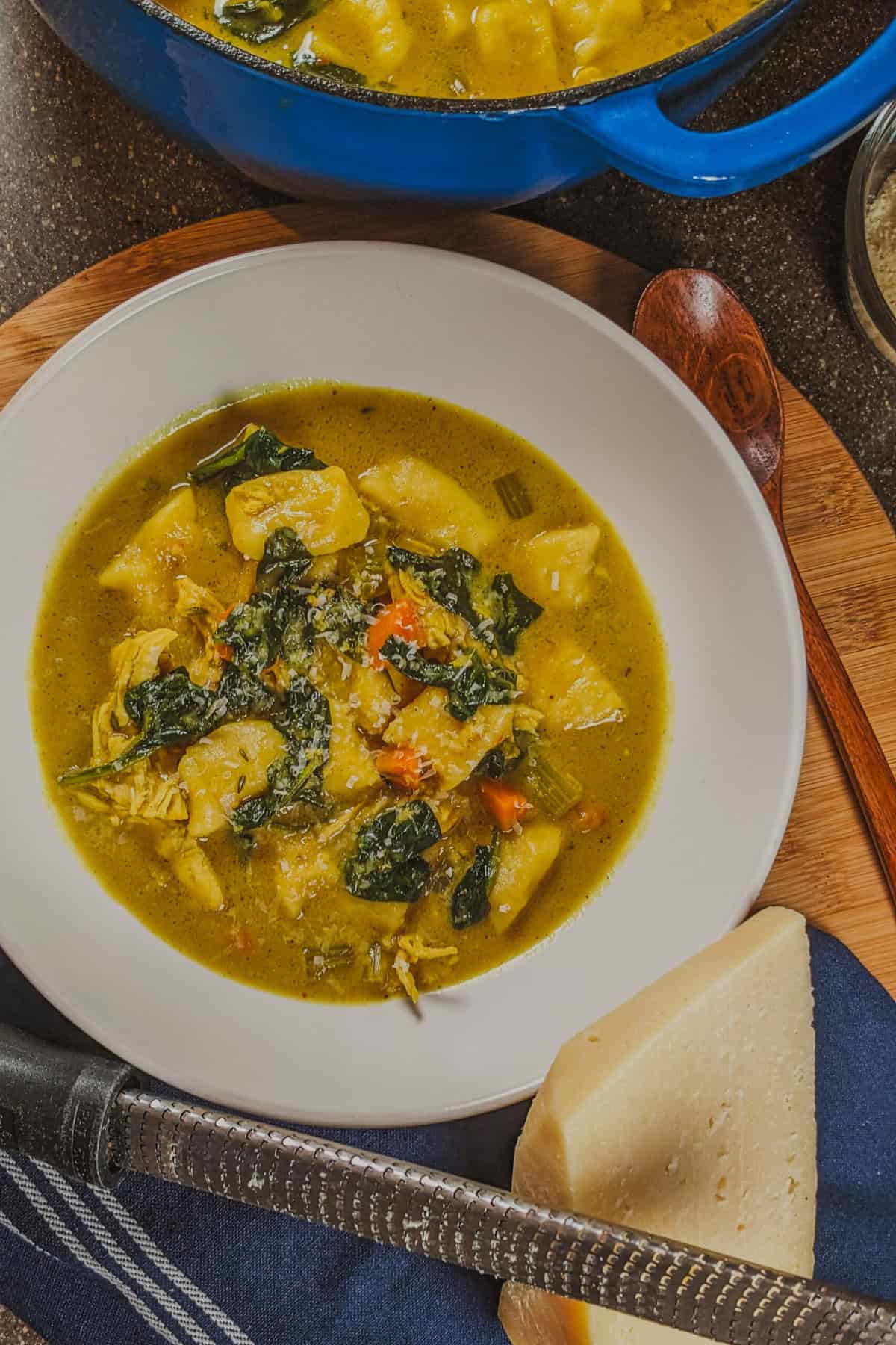 Vibrant curry coconut chicken gnocchi soup next to a block of parmesan cheese and a microplane grater on a wooden board.