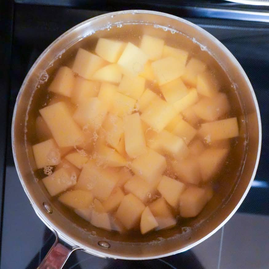 potato chunks boiling in a stainless steel pot on stovetop.