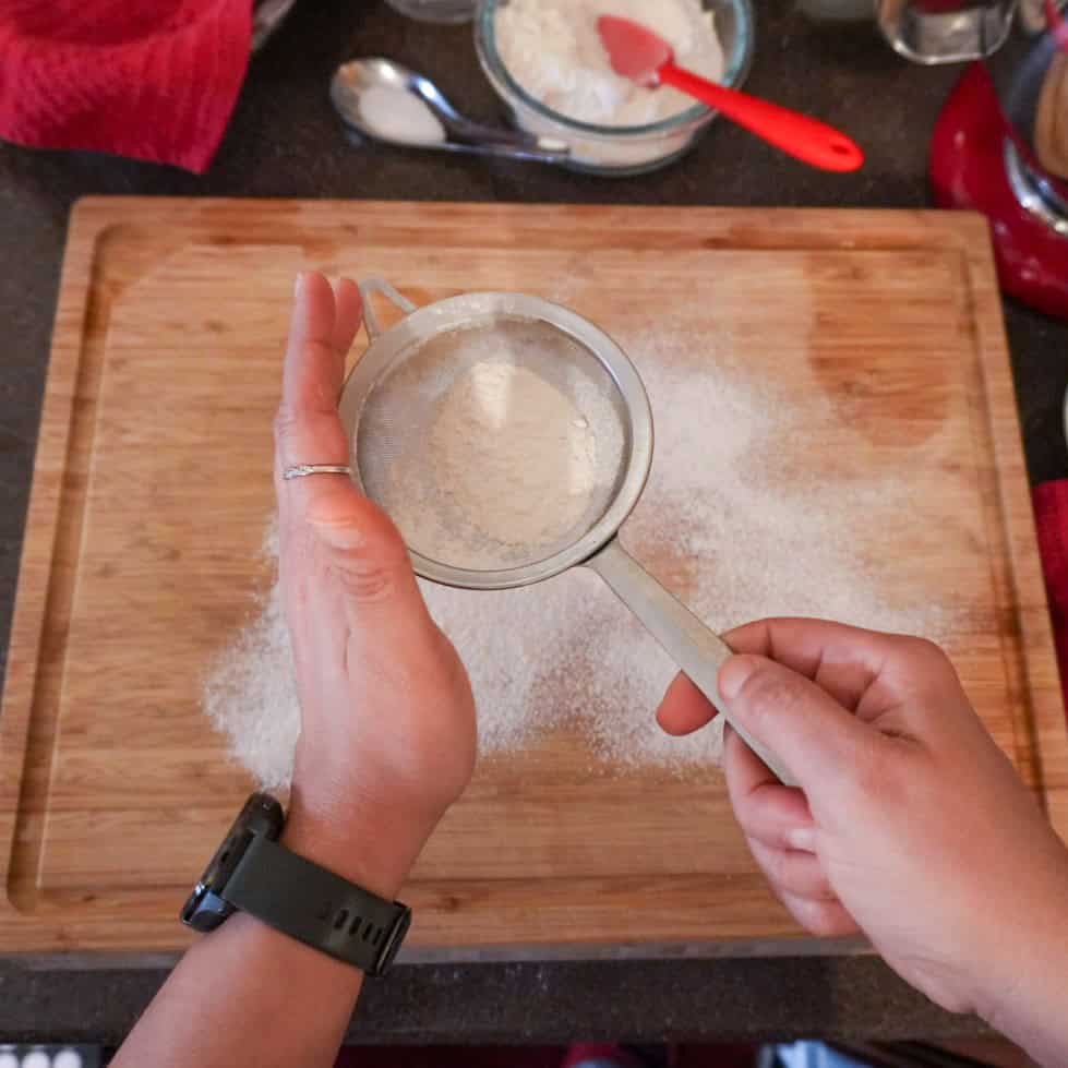 Sifting flour while preparing flavorful curry coconut chicken gnocchi soup in a cozy kitchen.