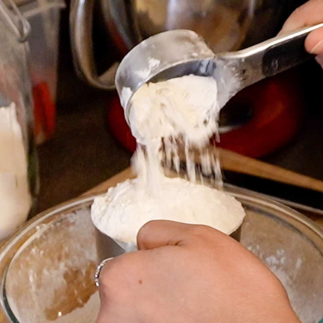 Measuring flour for potato gnocchi above bamboo cutting board in a cozy kitchen setting.