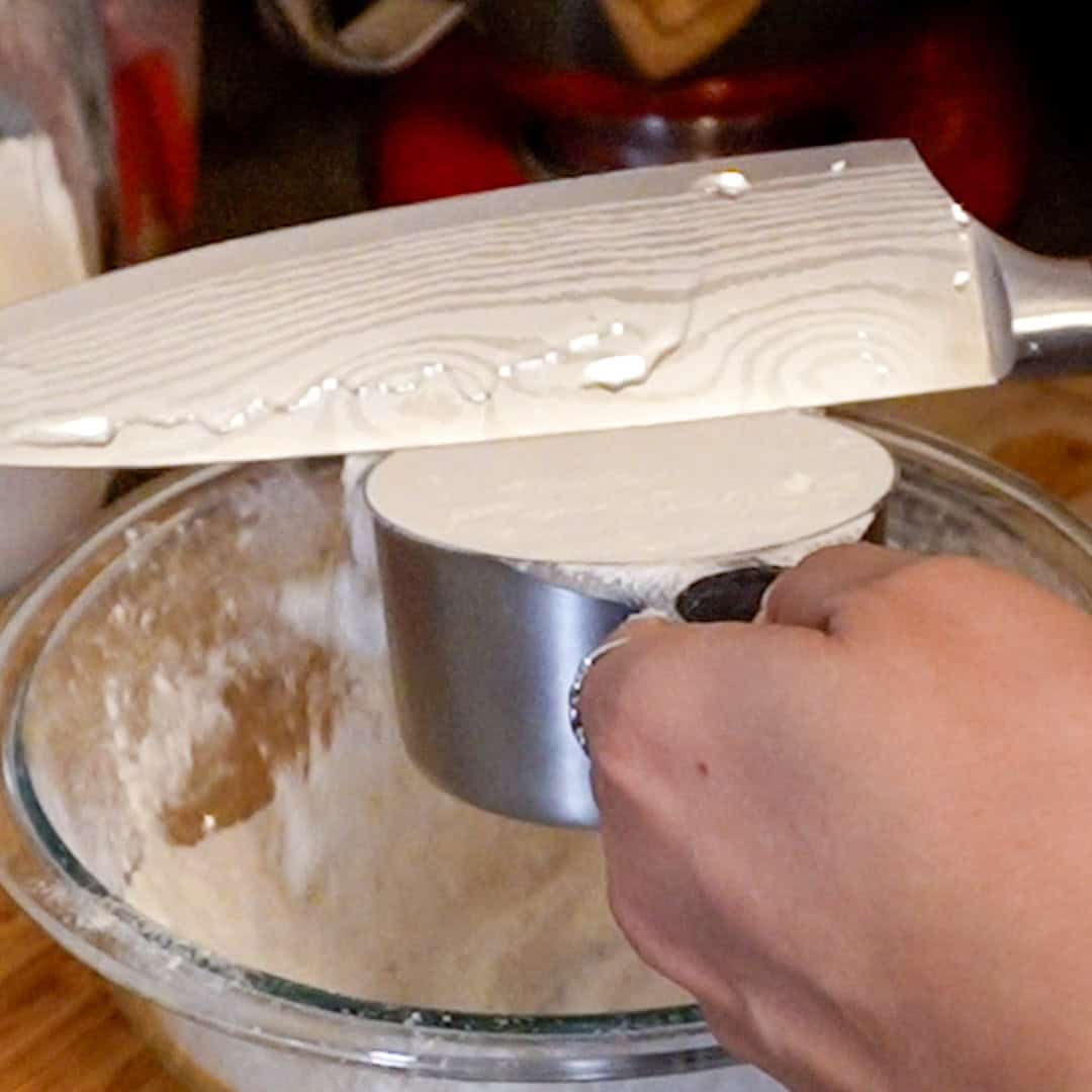 Measuring flour for potato gnocchi in a stainless steel cuisinart measuring up and a paudin chef knife in a vibrant kitchen setting.