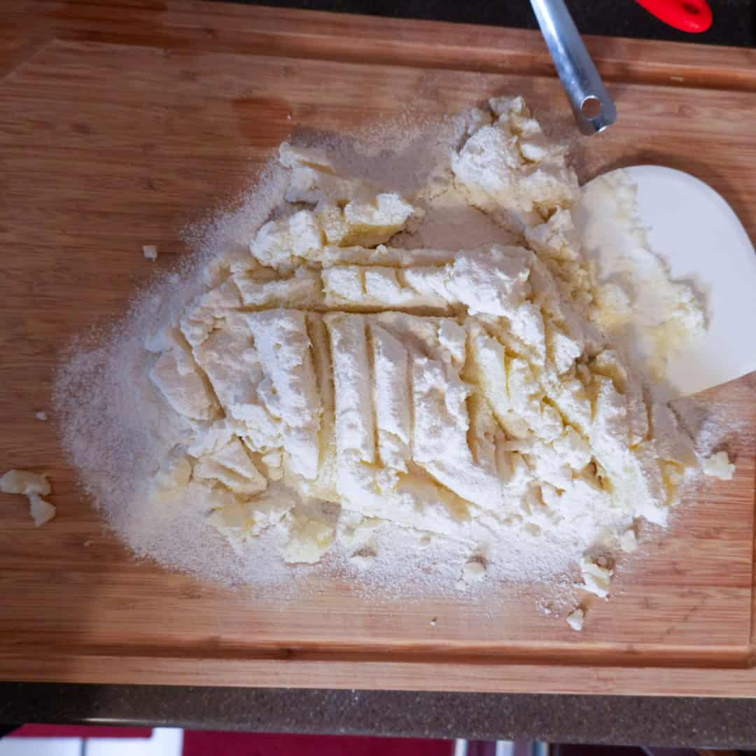 Flour mounds prepared for potato gnocchi on a wooden cutting board.