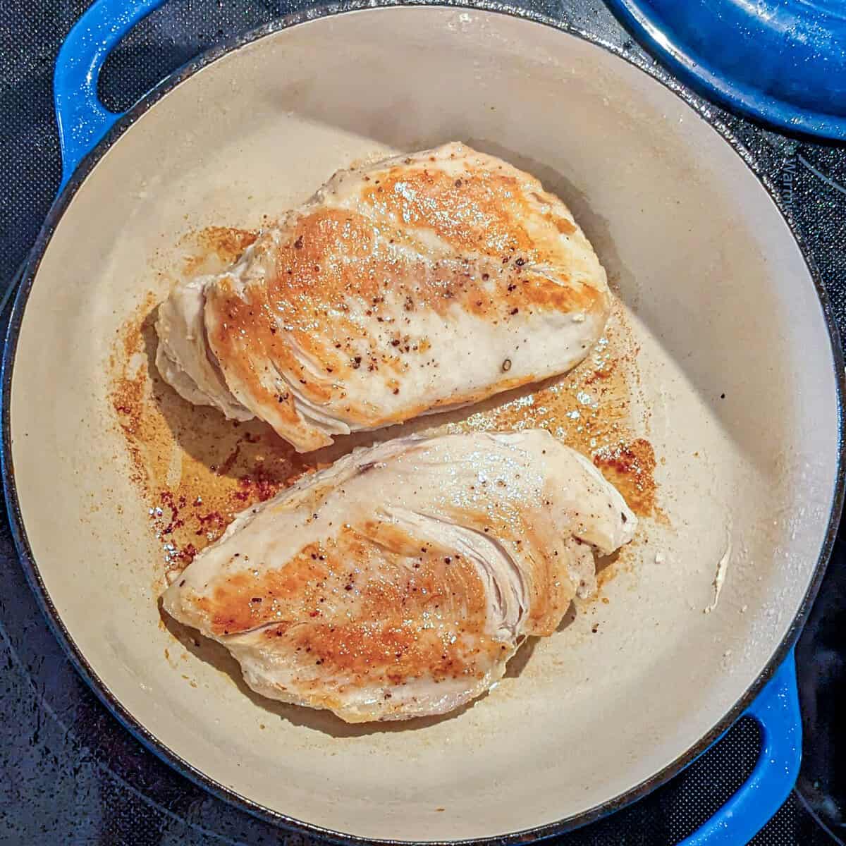 Golden-brown chicken breasts searing in a cast-iron skillet for a delicious Curry Coconut Soup.