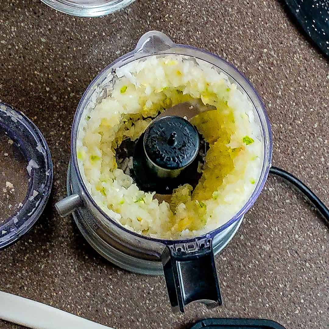 Freshly chopped onions in a food processor, ready for curry coconut chicken gnocchi soup.